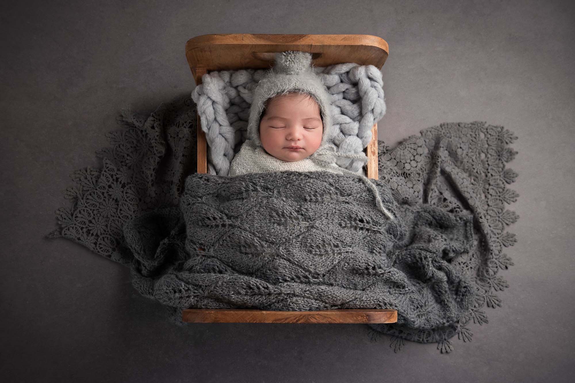 newborn little boy in a tiny bed with grey blanket