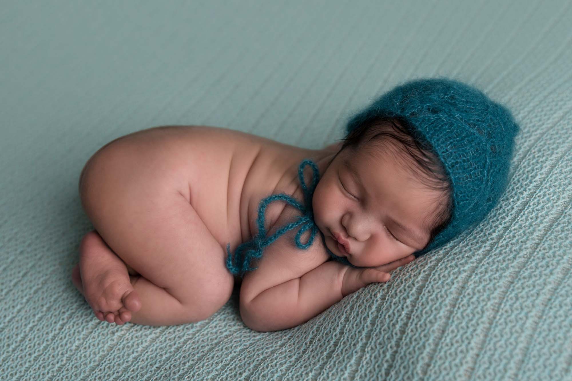 newborn little boy is in bump up pose in green hat on a green blacket