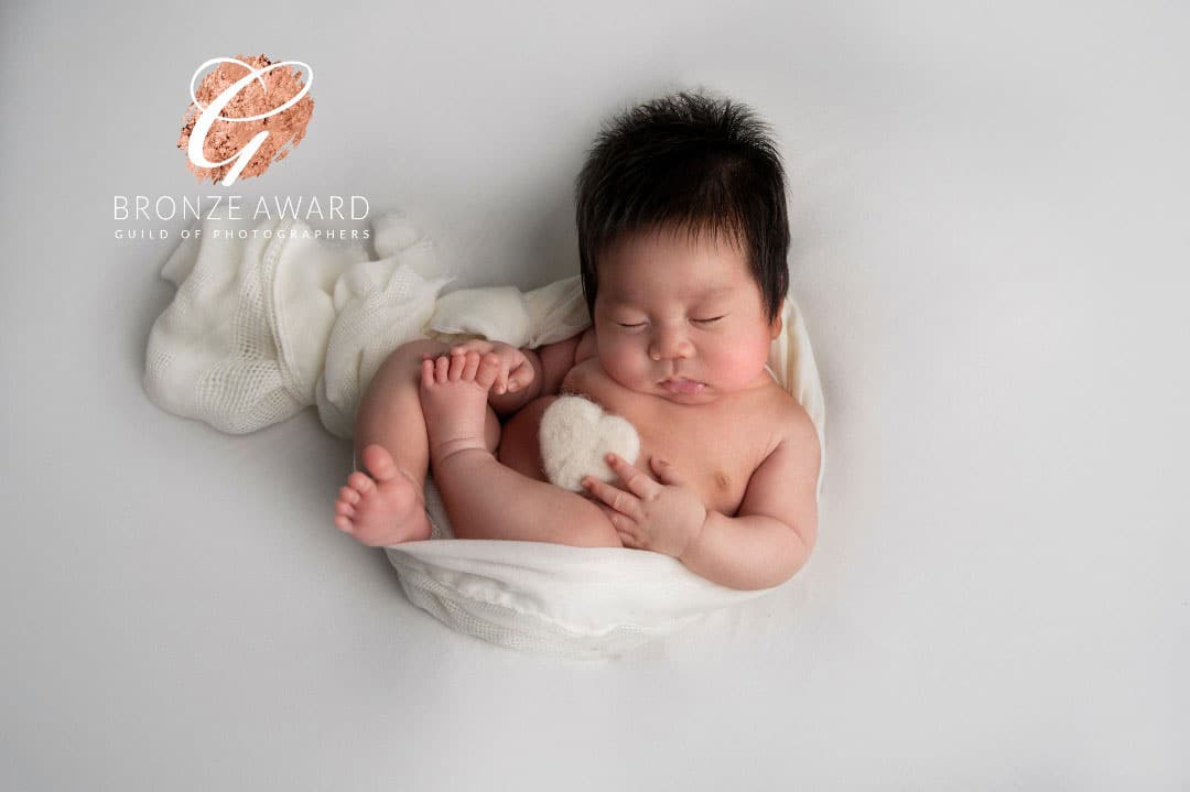 newborn baby in white wrap and white heart photographed by Newborn Photographer Manchester