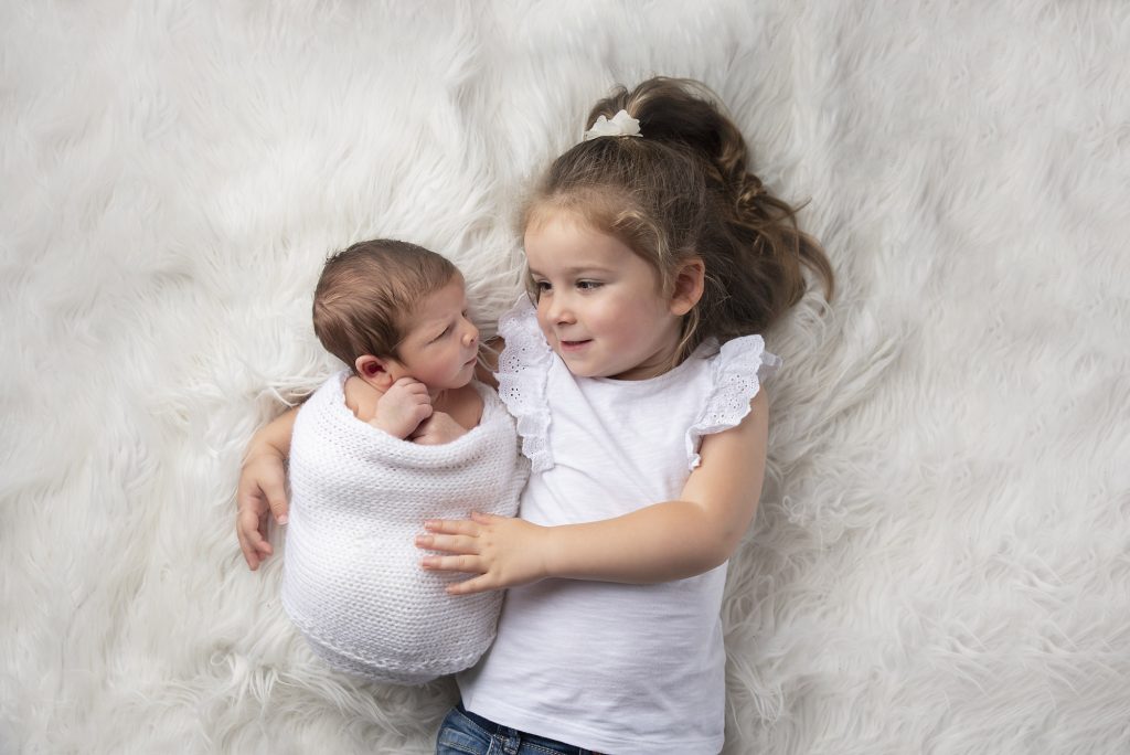 siblings on white fur photographed by Newborn Photographer Manchester