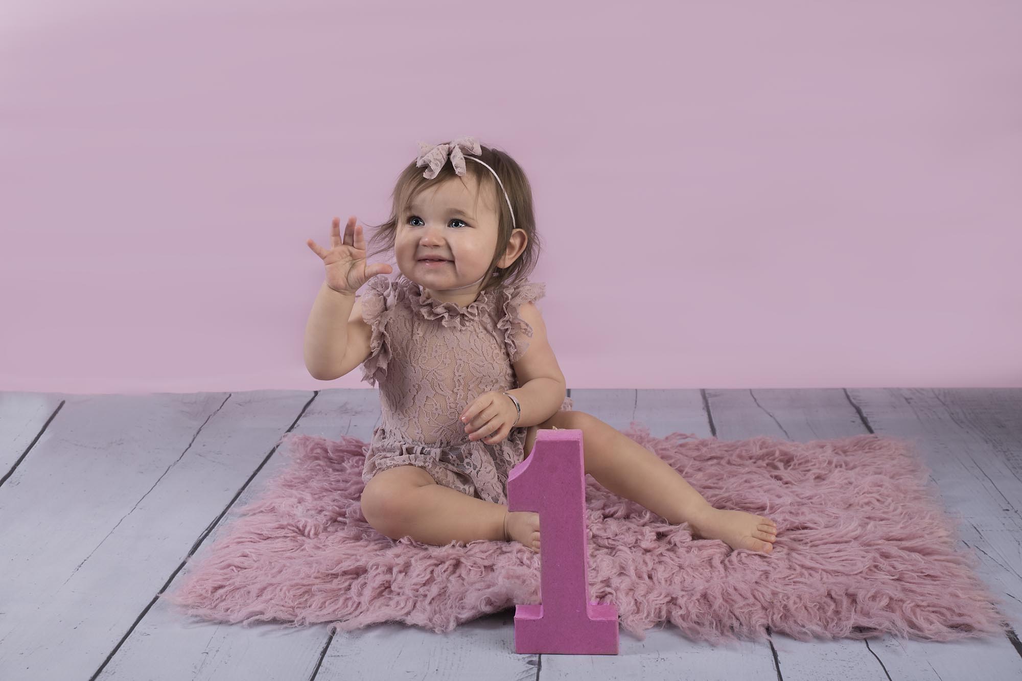 toddler girl is sitting on a pink fur and smiling photographed by Baby Photographer Manchester