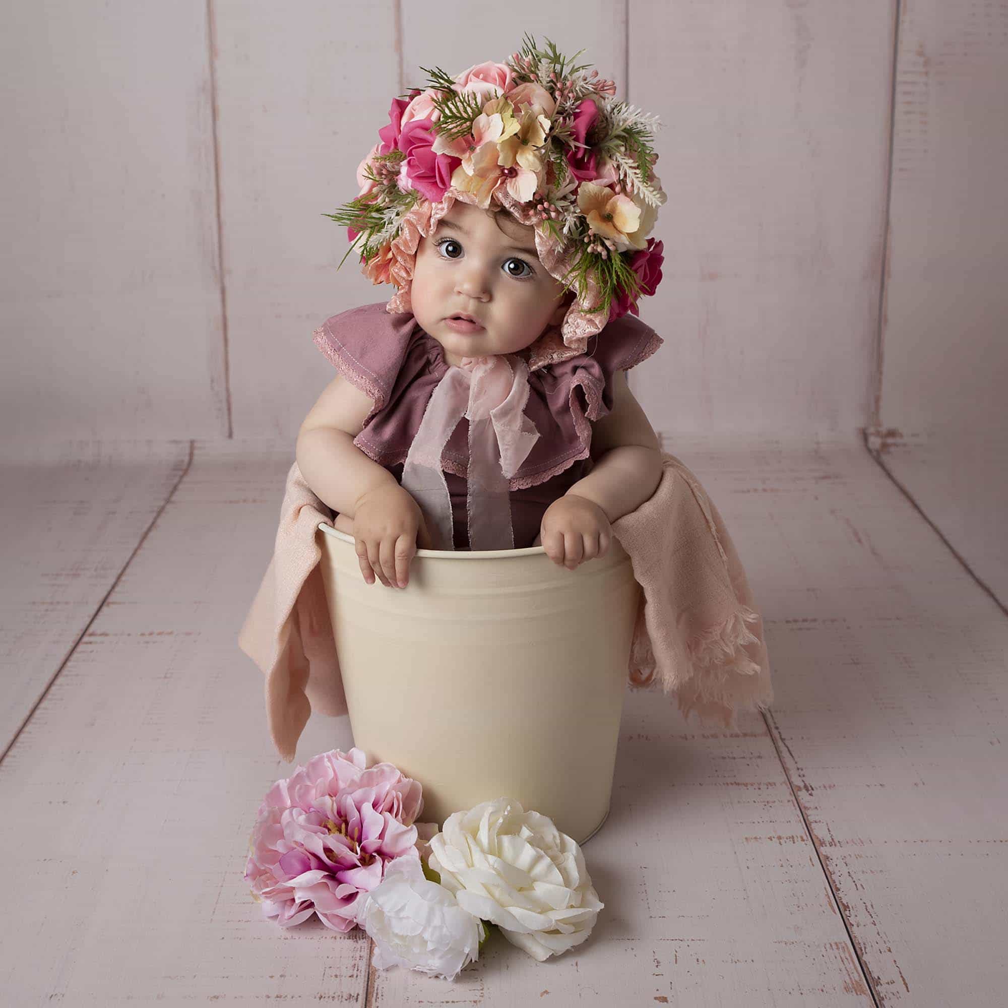 little girl is sitting in a bucket with flower bonnet photographed by Baby Photographer Manchester