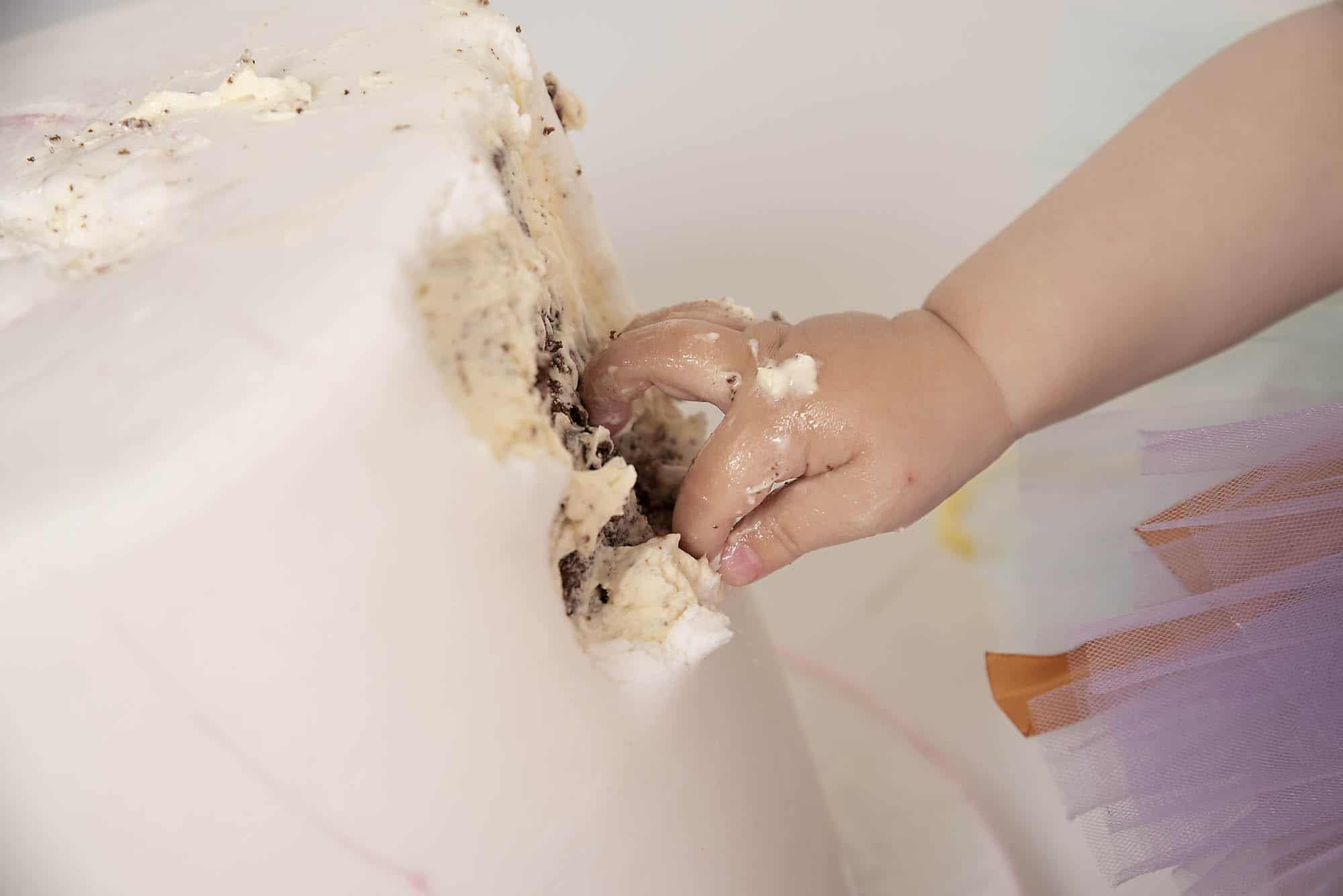 smashing cake with tiny hand photographed by cake smash photography Manchester