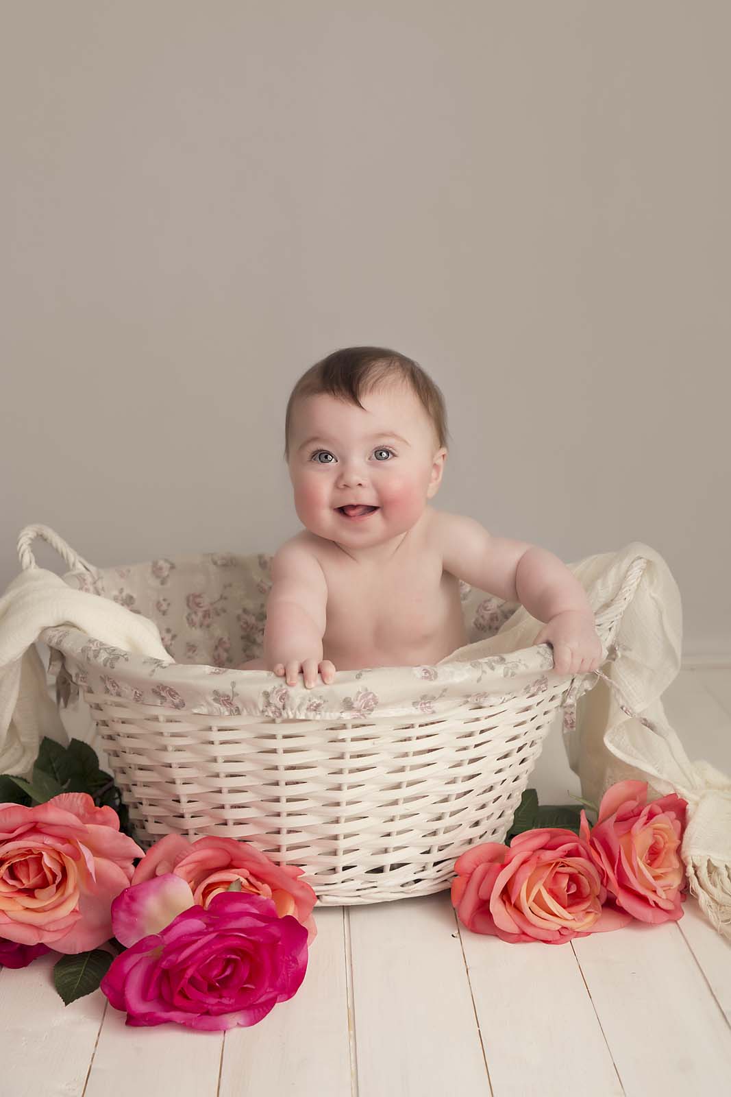 baby girl is sitting in a whit basket with pink roses photographed by baby photogrepher Manchester