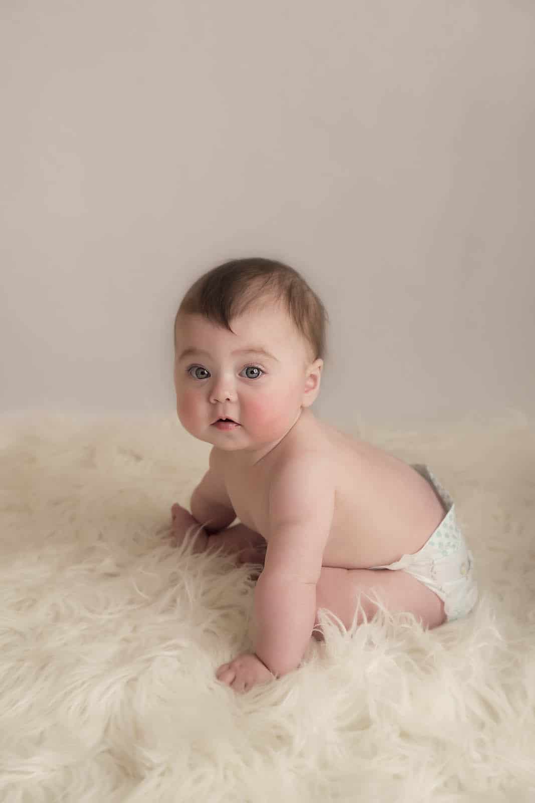 baby is sitting on a white fur photographed by baby photographer Manchester