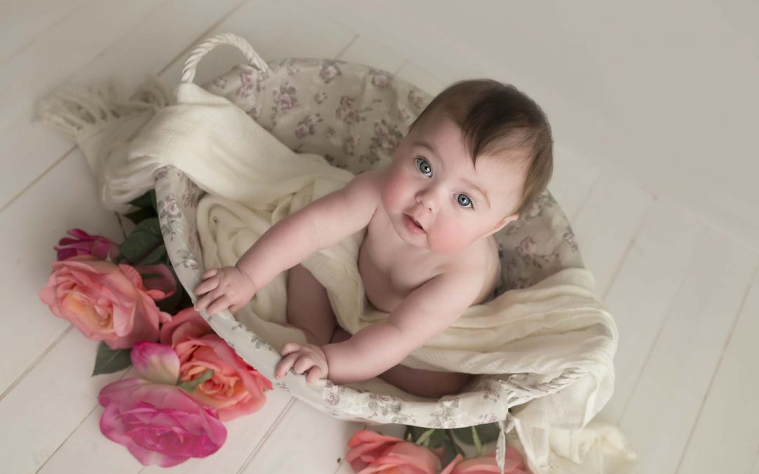 baby is sitting in a white basket with flowers photographed by baby photographer Manchester