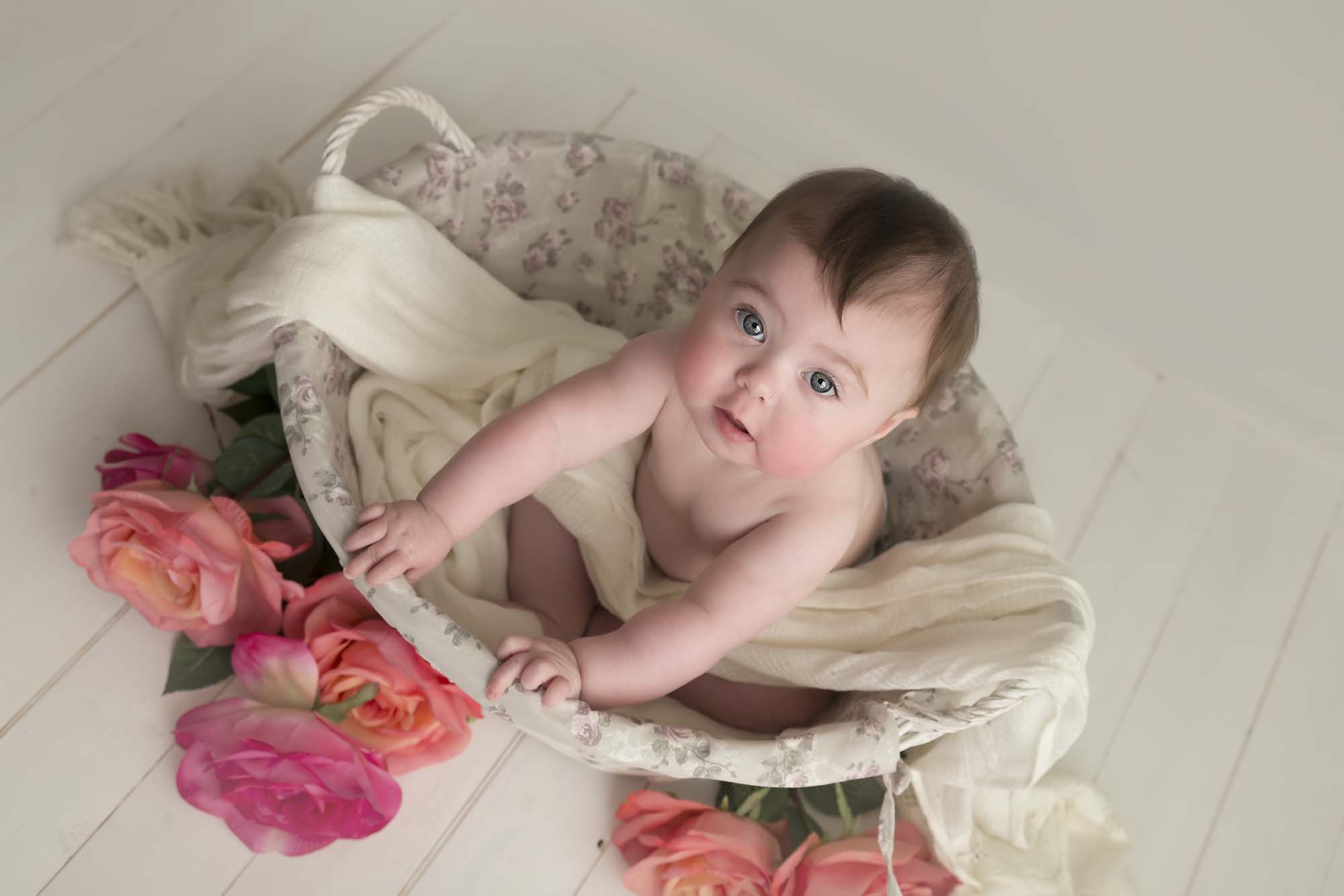 baby is sitting in a white basket with flowers photographed by baby photographer Manchester