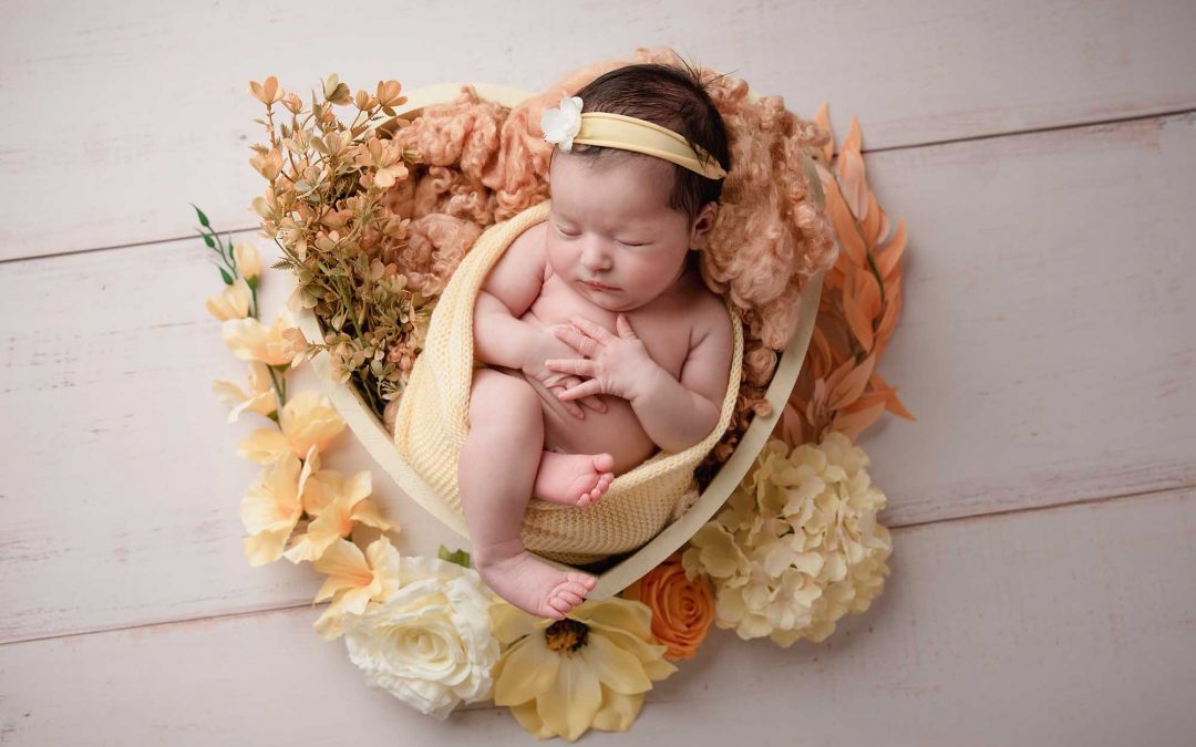 newborn girl with hear shape bowl and flowers taken by newborn photography Manchester
