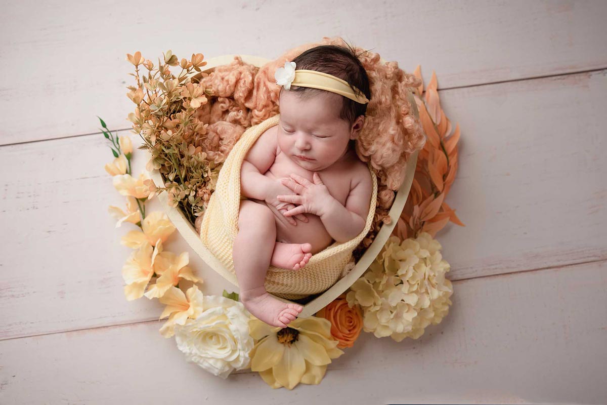 newborn girl with hear shape bowl and flowers taken by newborn photography Manchester