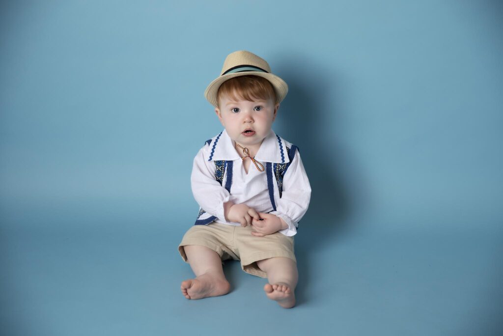 sitter session with a one year old boy sitting by a blue background in a baby photography studio in manchester