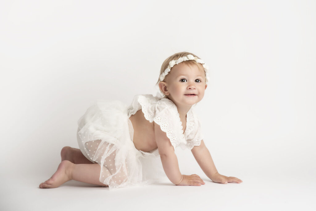 one year old baby crawling in white romper smiling in a baby photography studio in Manchester