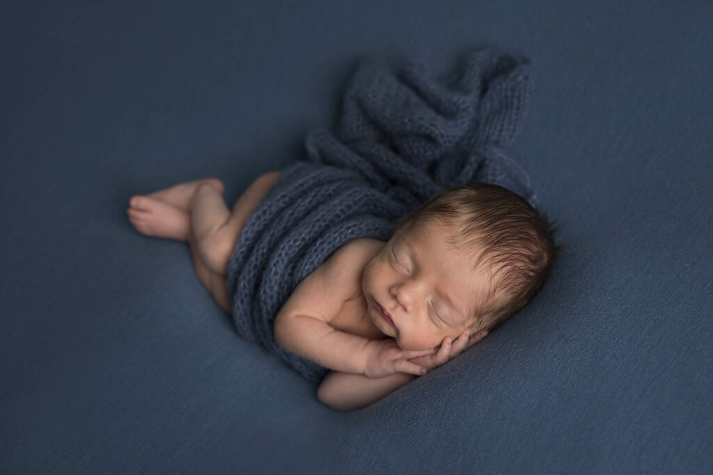 newborn baby in a side pose ona blue background and blue wrap