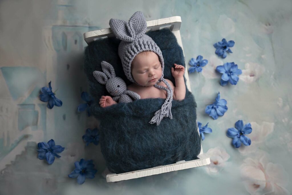 newborn on a bed with bunny hat and blue flowers