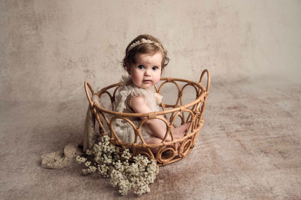 sitter baby in a basket with creamy background in a baby photography studio