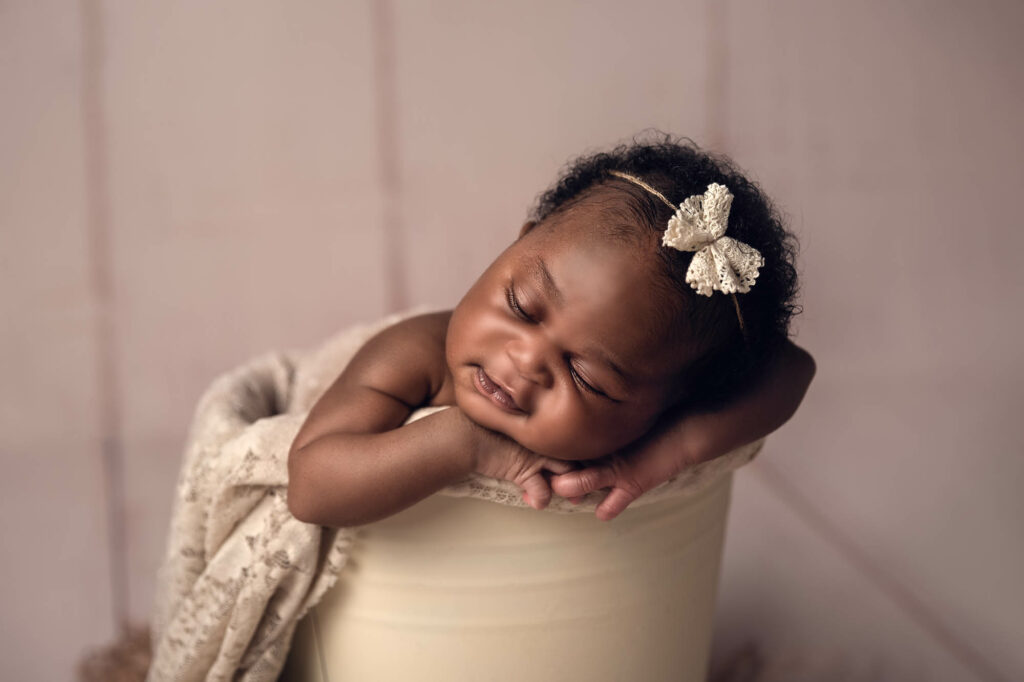 newborn photography session with a gorgeous little girl chin up on a cream bucket sleeping