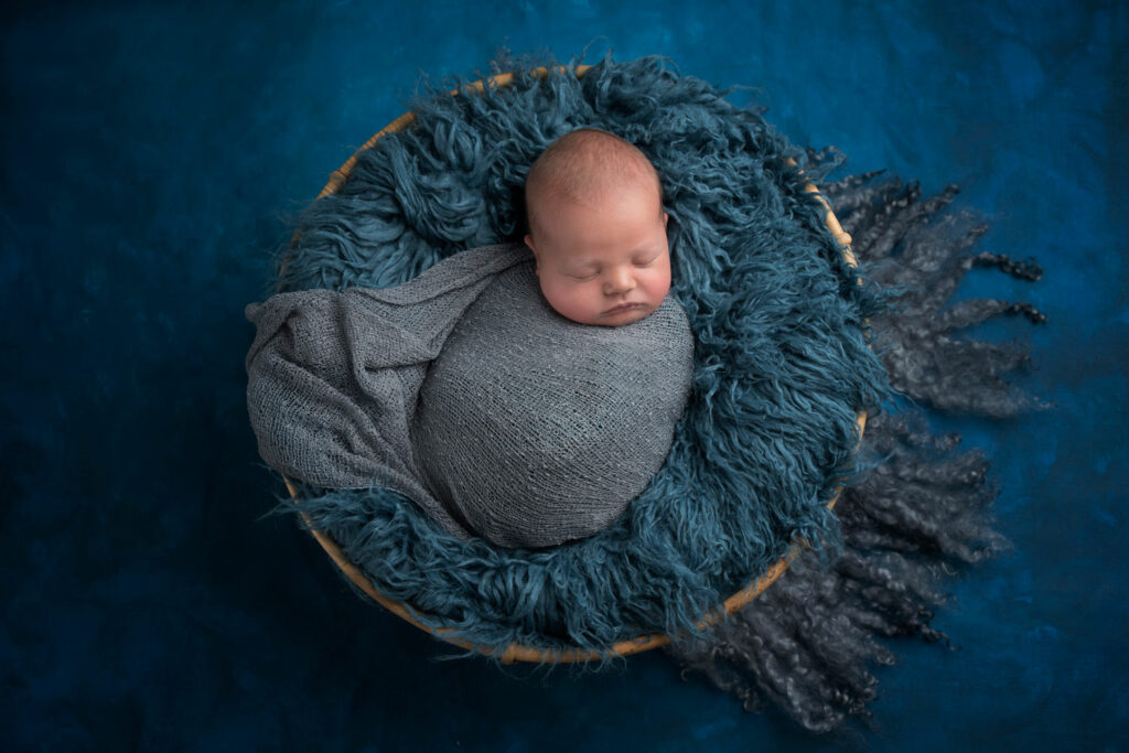 newborn baby sleeping in blue fur basket wrapped taken by newborn Photographer Dora Horvath Photography